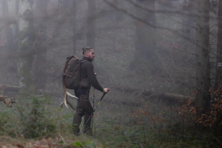 Mężczyzna z plecakiem idzie przez zamglony las. Na plecaku zawieszona jest tyka jelenia, fot. Daniel Pękalski